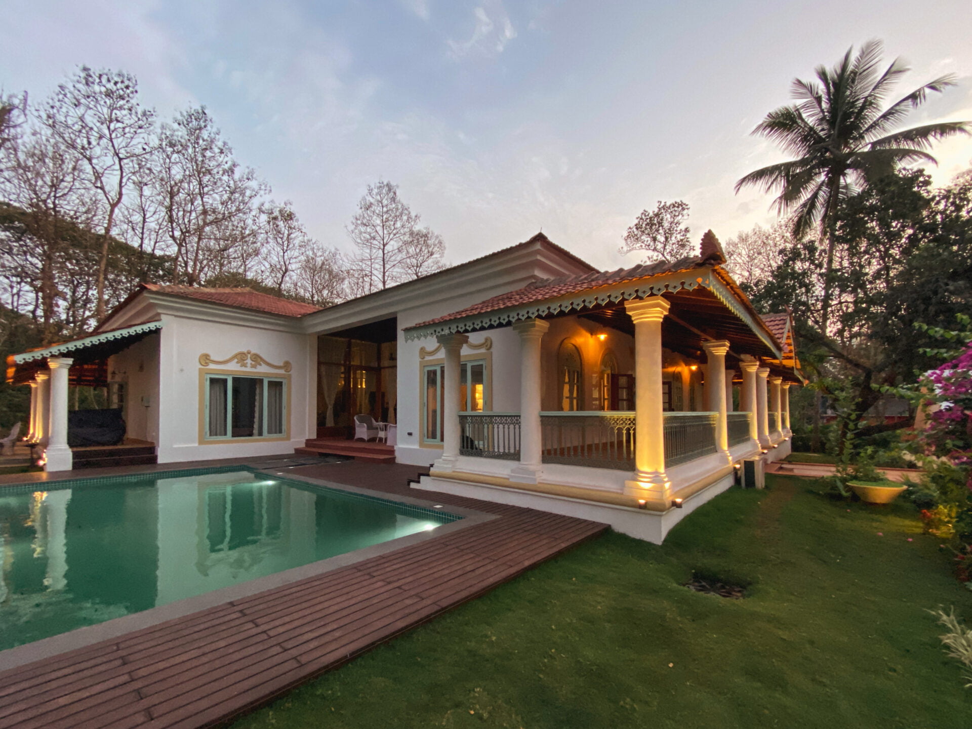 A neo-classical villa set within a landscaped garden, where colonnaded verandahs, warm lighting, and a reflective pool create a composed and elegant residential setting.