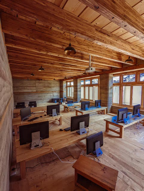 Light and learning: Large windows flood the workspace with natural light, illuminating the natural grain of the wooden floors and the layered earth walls.