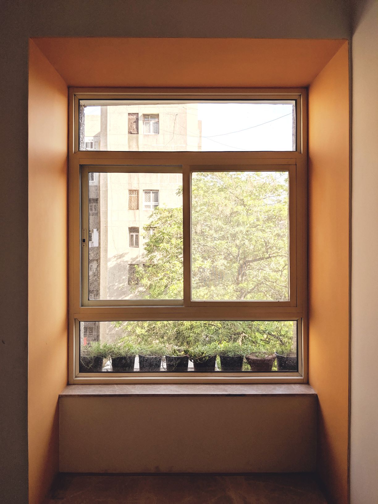 Framed Perspectives: A bold, deep orange window reveal acts as a picture frame, turning the everyday view of the neighborhood greenery into a vibrant focal point within the room.