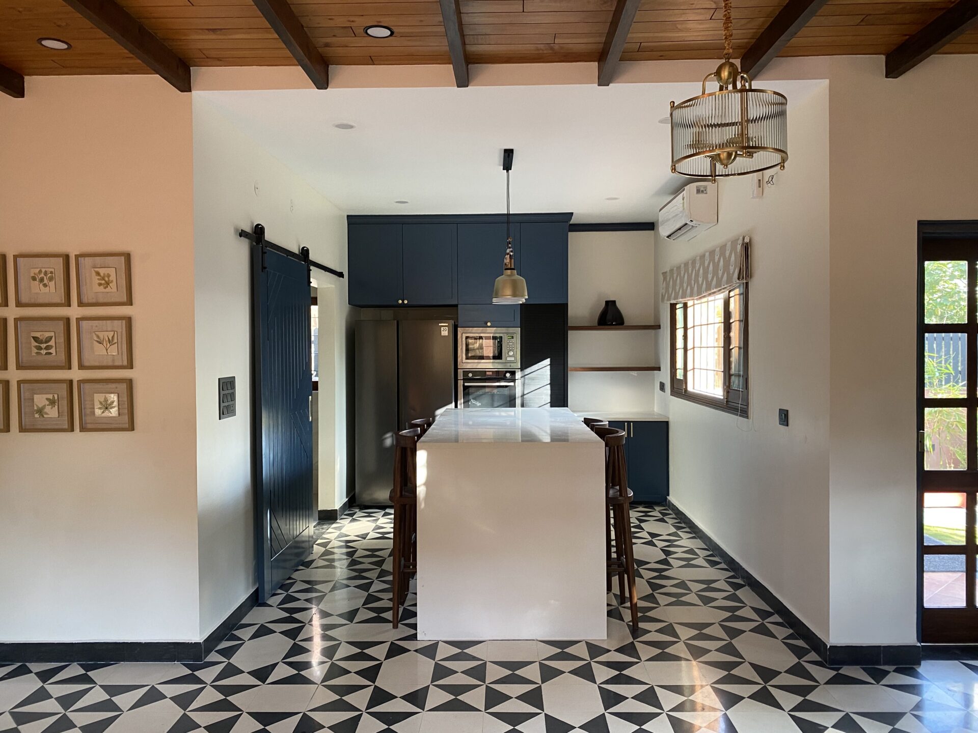Monochrome meets Indigo: The dramatic black-and-white geometric flooring is perfectly balanced by deep blue cabinetry and warm wooden ceiling beams.