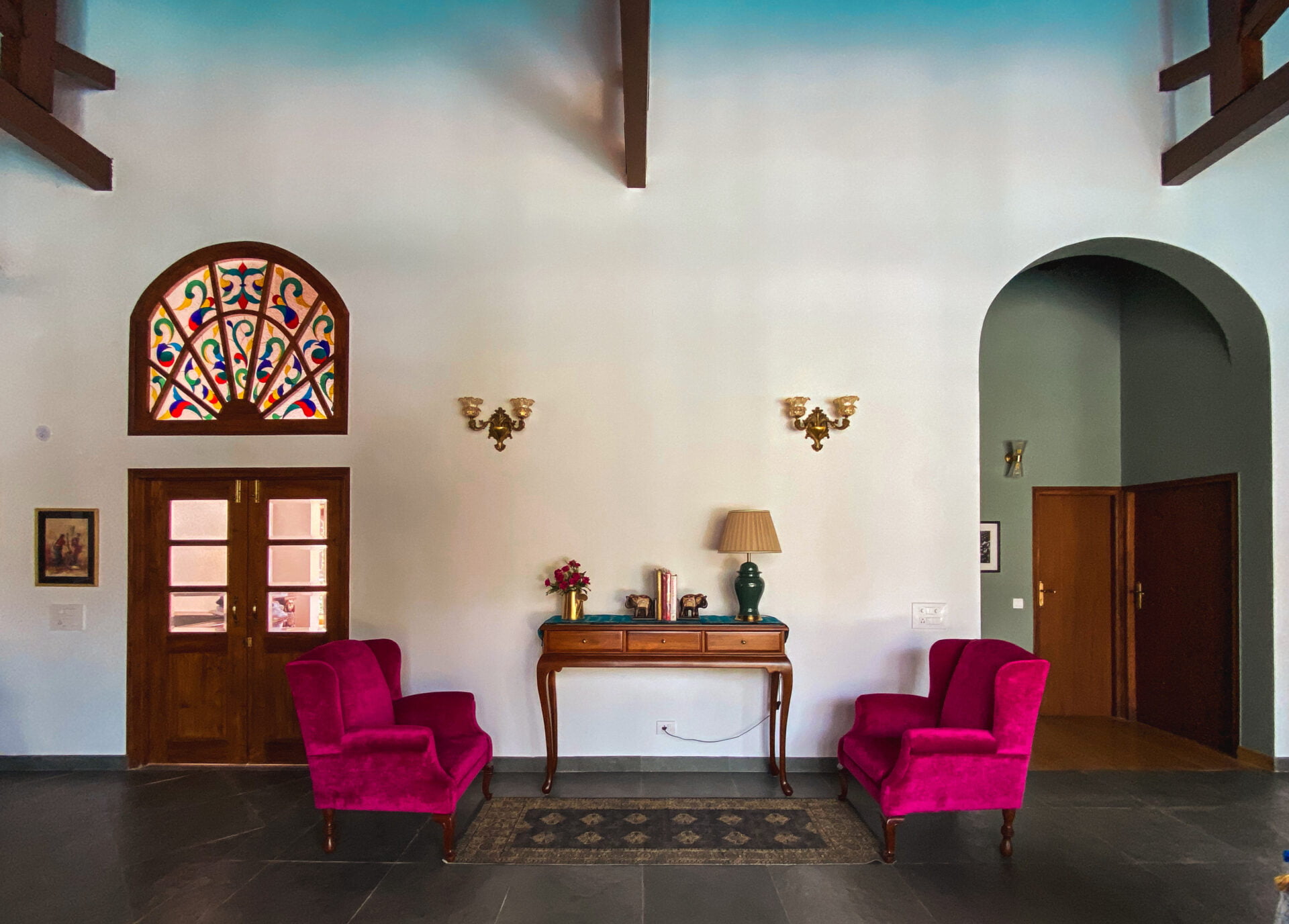 The spacious interior features a lofty ceilings with exposed beams, highlighted by vibrant magenta armchairs and a colorful stained-glass archway.