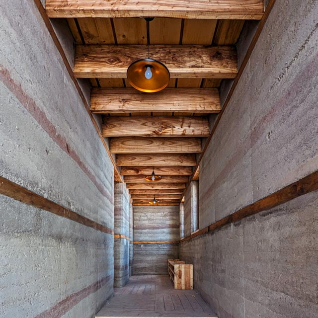 Textural rhythm: The corridor showcases the beautiful stratification of the rammed earth walls, perfectly framed by the repetitive wooden ceiling beams overhead.